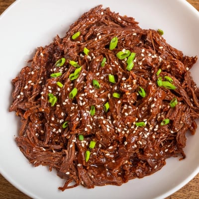 A fork-tender Slow Cooker Korean Beef dish garnished with sesame seeds and red chili, perfect for lettuce wrap assembly.  