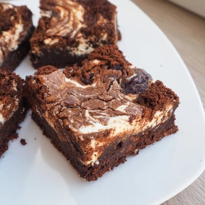 A single slice of Cottage Cheese Brownies rests on a white plate with crumbs and a chocolate drizzle.