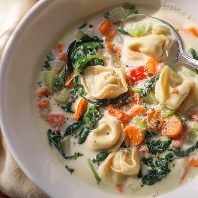Steaming bowl of comforting creamy tortellini soup featuring cheese-filled pasta and wilted spinach