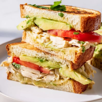 Warm grilled chicken avocado melt sandwich cut in half revealing layers of creamy avocado and provolone cheese