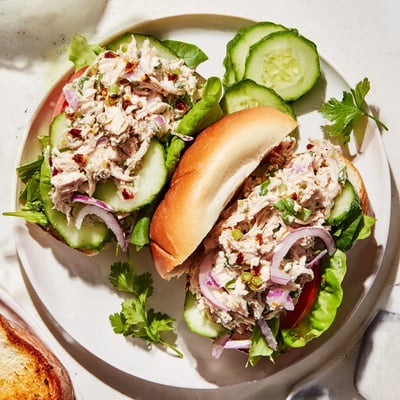 Open-faced chicken salad sandwich featuring chili crisp topped chicken breast, ripe tomato, and crunchy celery on a soft sandwich roll.