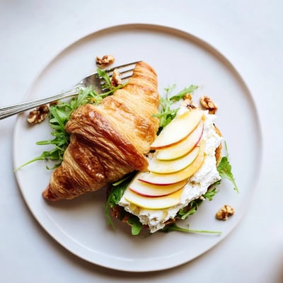 A lightly toasted Apple Goat Cheese Croissant Sandwich served with honey drizzle