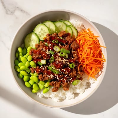 Savory hot honey ground beef bowl topped with colorful carrots cucumber and sesame seeds