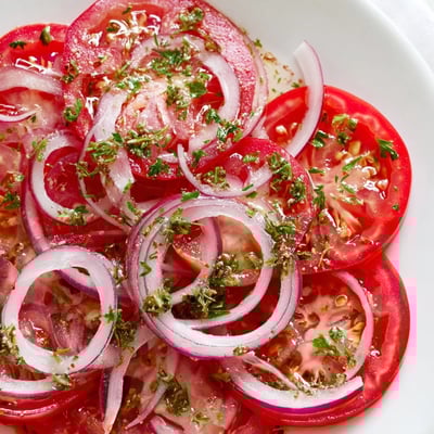 Crisp tomato and onion salad layered with chopped parsley glistening under olive oil dressing on serving platter