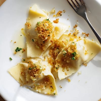 Creamy leek burrata triangoli plated on a white dish with herb-flecked golden crumbs