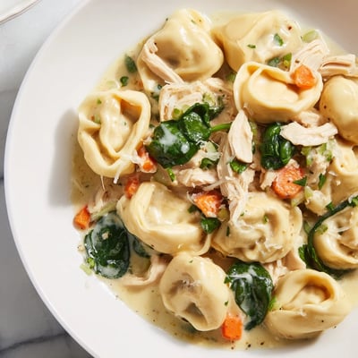 Slow cooker chicken tortellini topped with Parmesan and fresh parsley in a steaming bowl